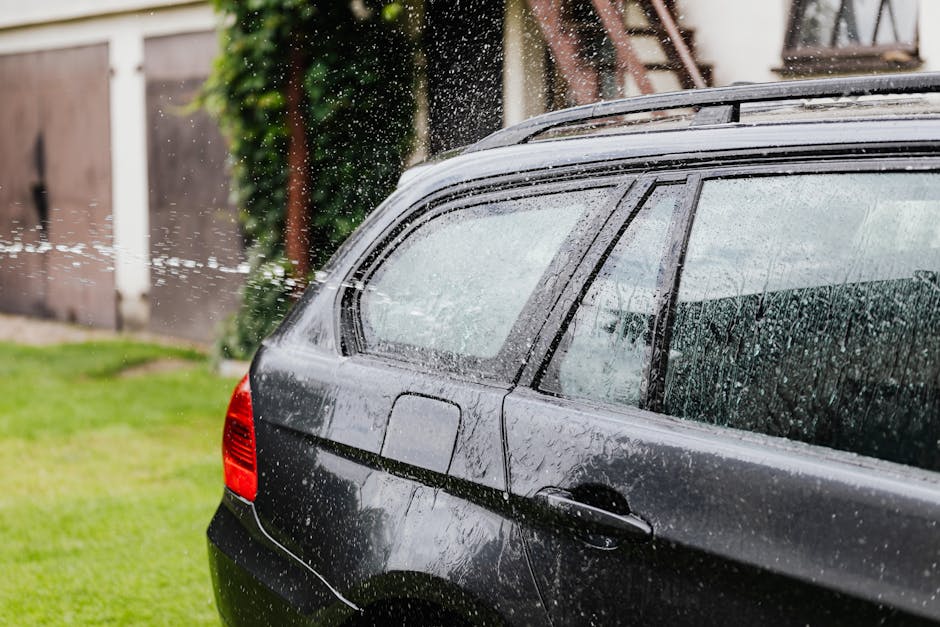 Side view of a black car being washed with water spraying in an outdoor setting.
