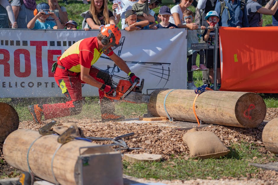 Chainsaw wielding lumberjack competing in woodcutting event outdoors with crowd watching.