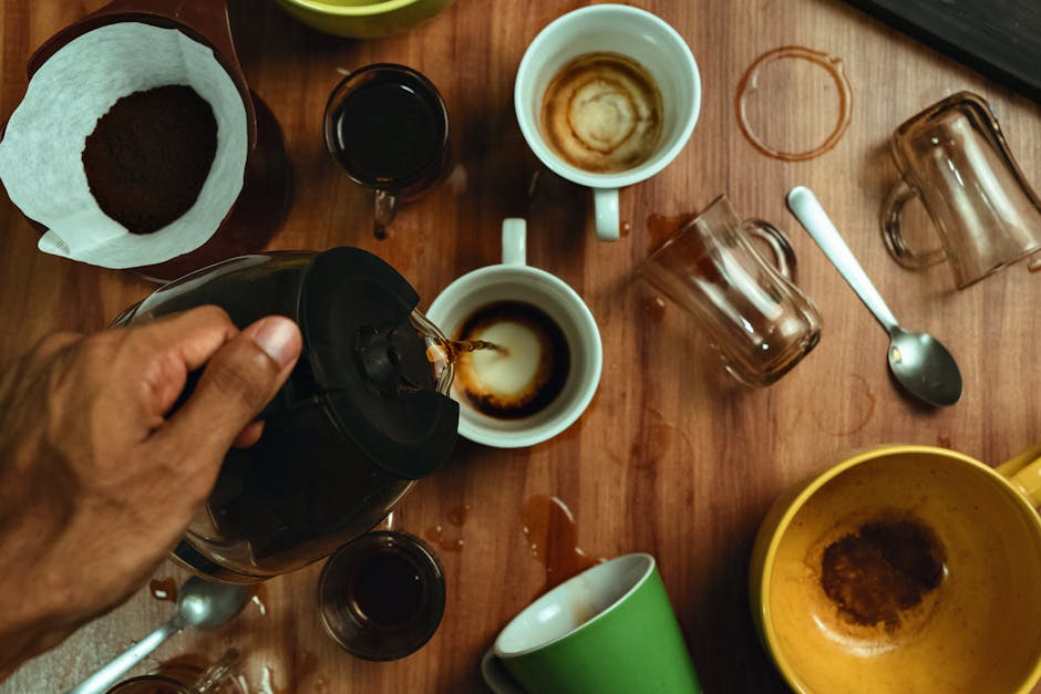 Top view of a hand pouring coffee into assorted mugs on a wooden table.