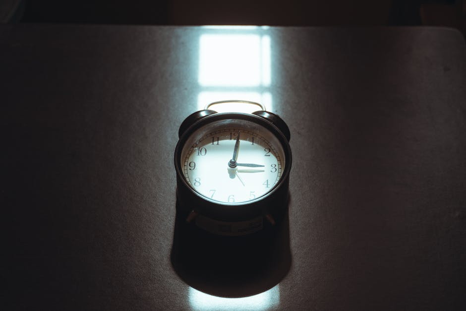 A classic vintage alarm clock casting artistic shadows on a desk surface with moody lighting.